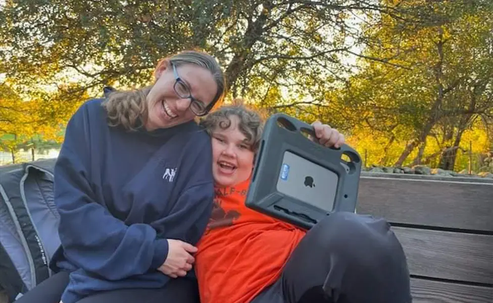 Pamela Whynot, BCBA, smiling with a young client outdoors using an AAC device for ABA services Massachusetts