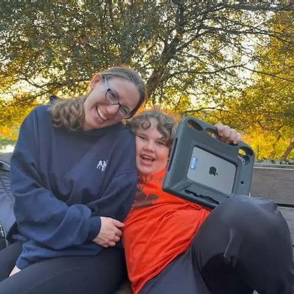 Pamela Whynot, BCBA, smiling with a young client outdoors using an AAC device for ABA services Massachusetts